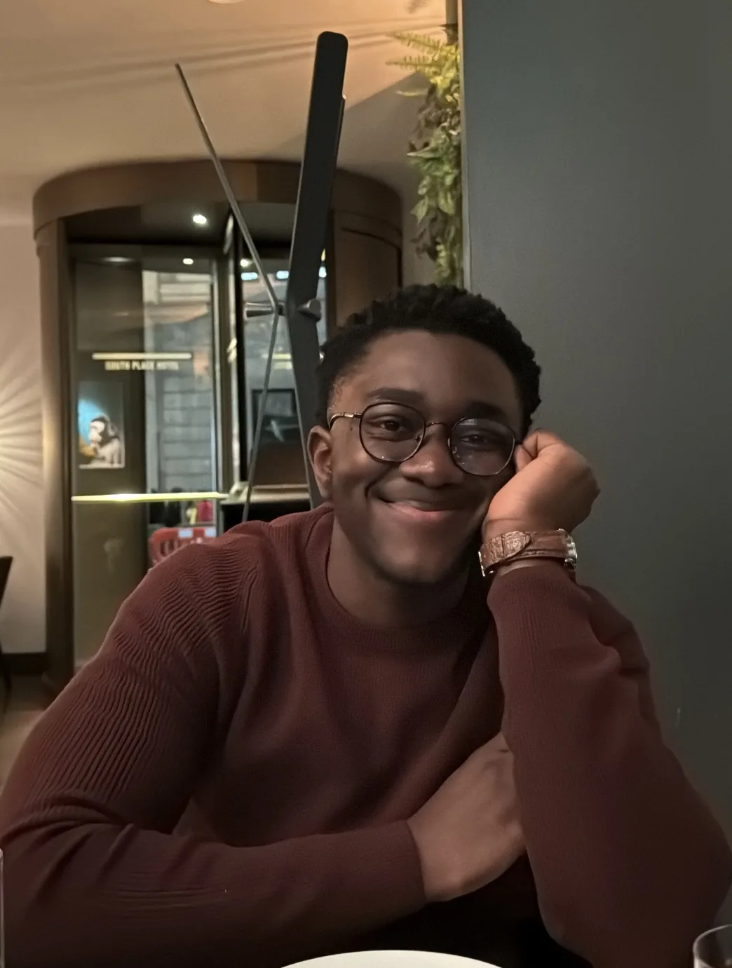 Yooku Obiri, in round glasses and a dark button-up shirt, smiling — a black-and-white studio portrait.