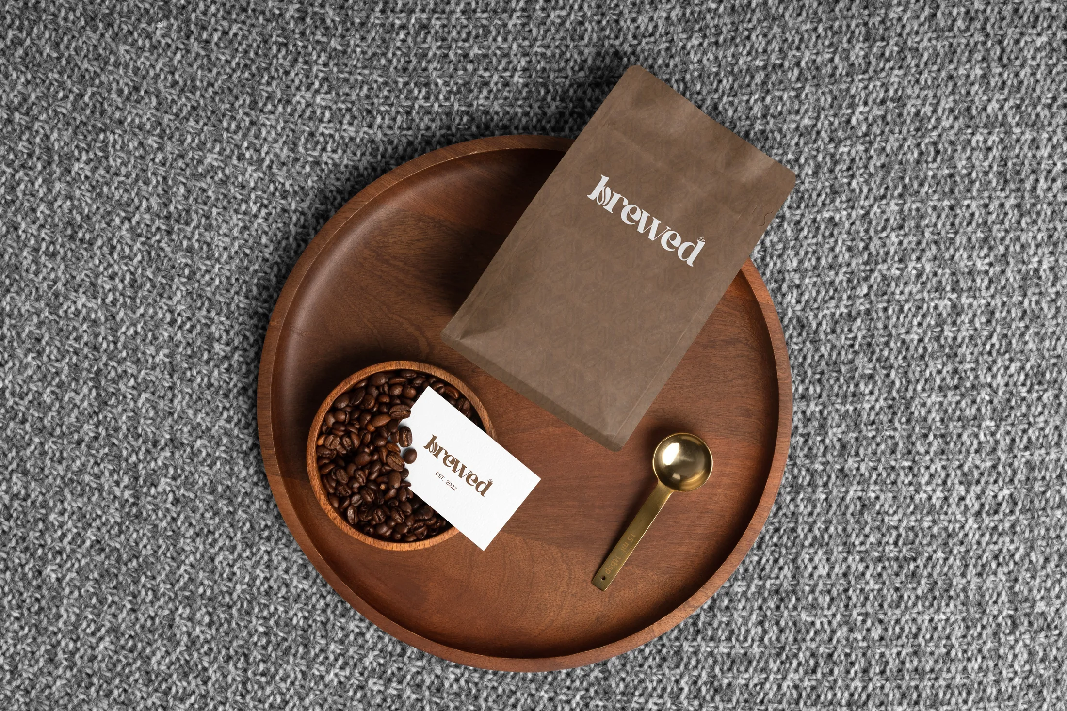 Brewed brand flat-lay — a kraft coffee bag, a business card and a bowl of beans with a gold spoon on a wooden tray.